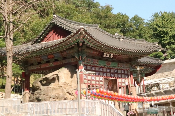 보도각이라 현판이 걸린 전각 안에서 밖을 내다보는 듯한 '옥천암 마애보살'.  전각 왼쪽으로 마애불을 품은 큰 바위가 보인다. [사진 강나리 기자]