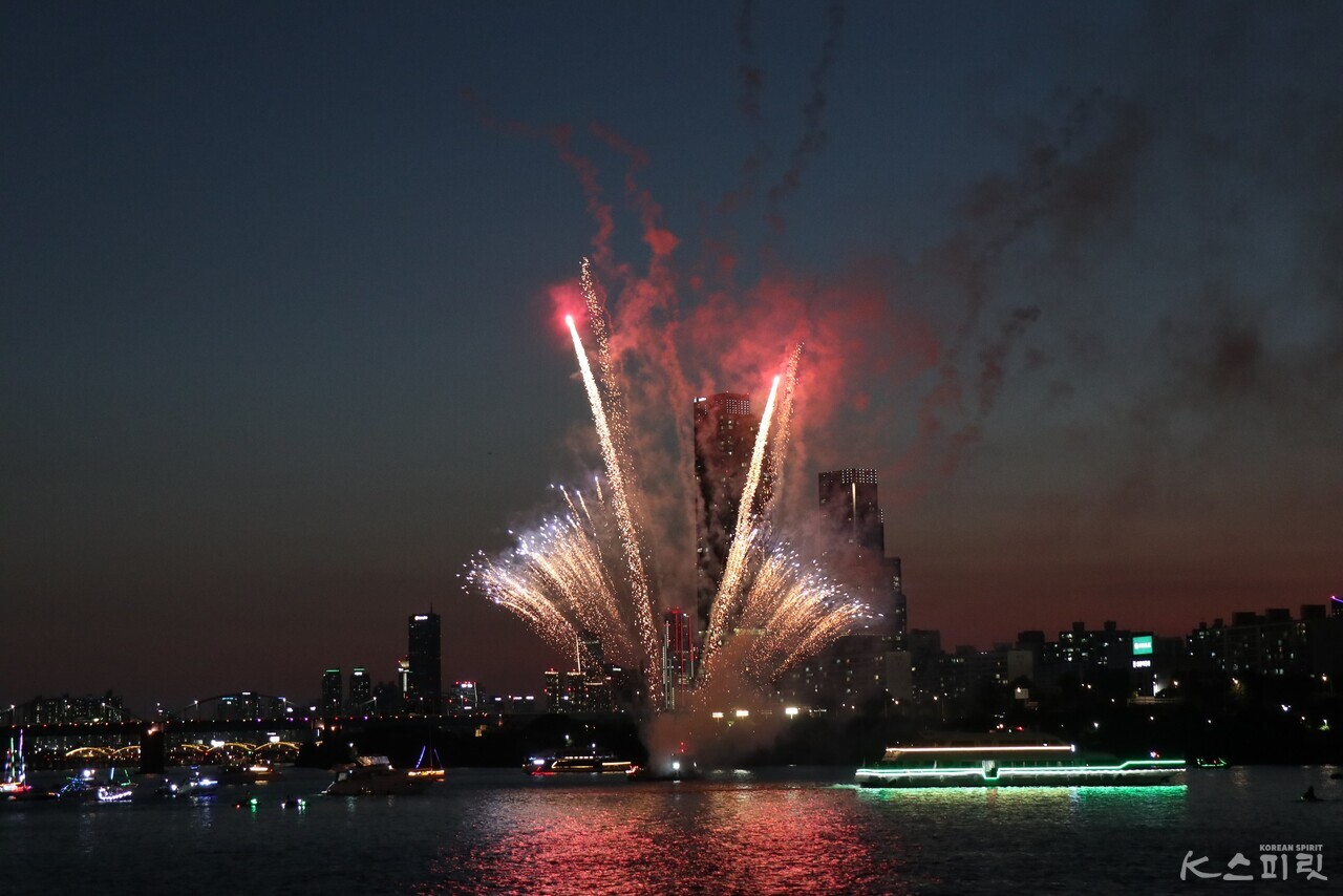 불꽃놀이 속 우렁찬 기적소리와 함께 연두색 불빛을 뿜으며 대장선(오른쪽)이 잠수교 아래를 향해 출발하고 다양한 보트와 요트들(오른쪽)이 따랐다. 사진 강나리 기자.
